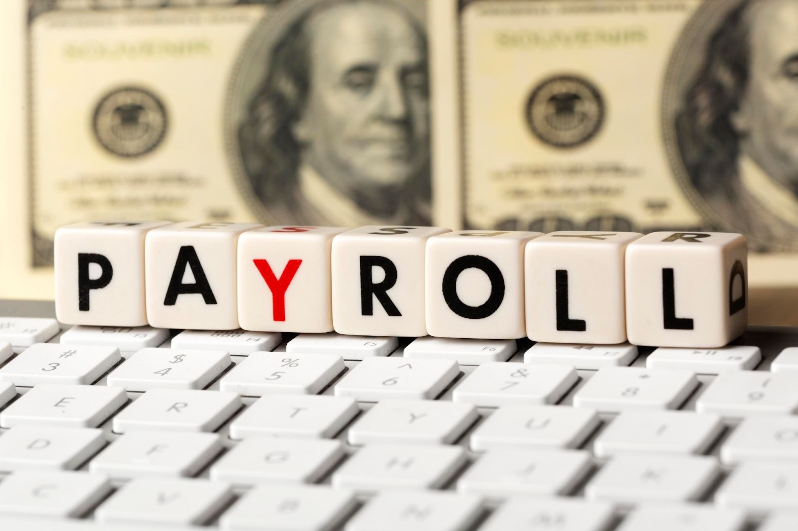 PAYROLL blocks on a calendar with hundred dollar bill background
