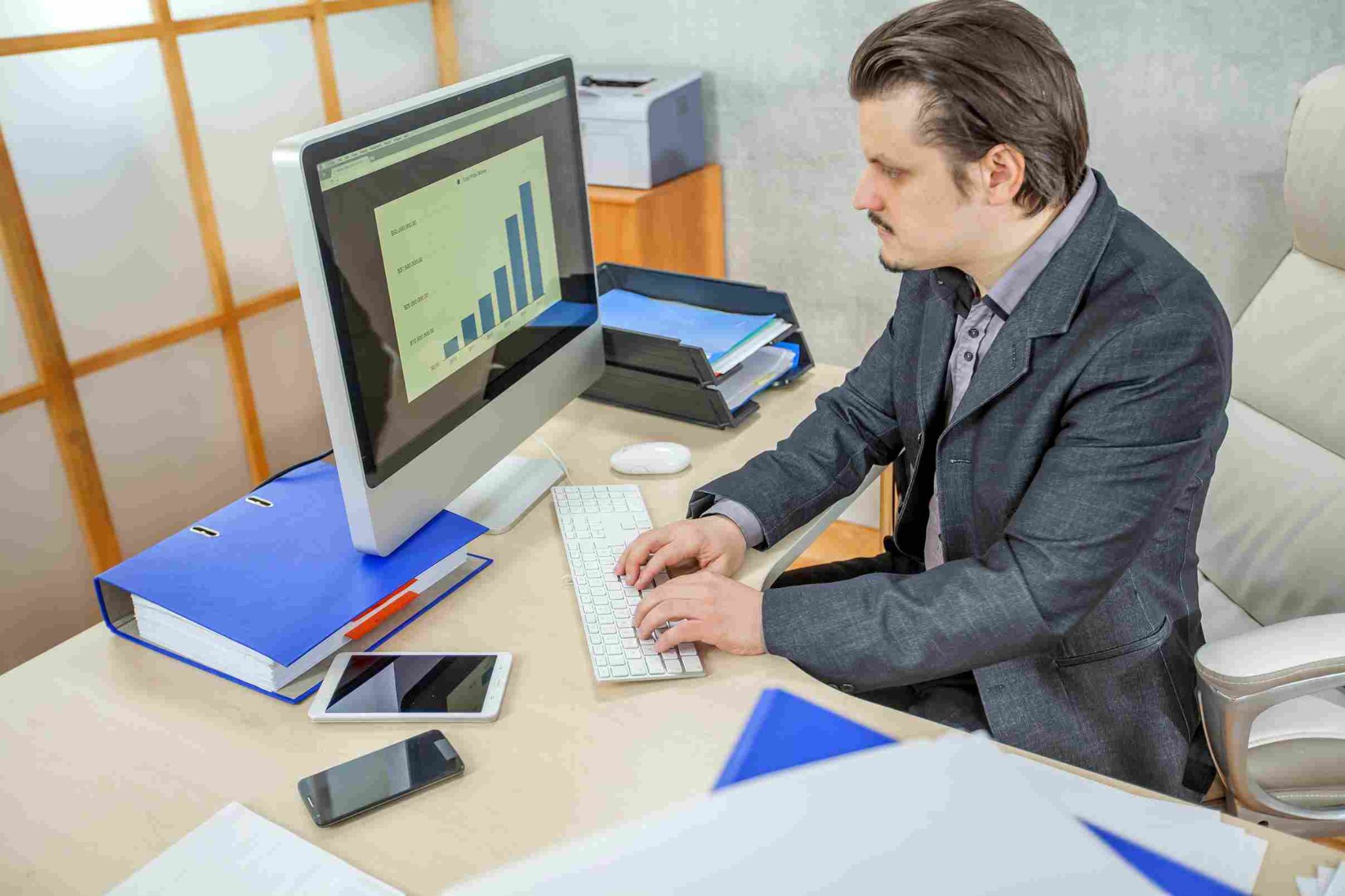 Man at desk looking at monitor with chart