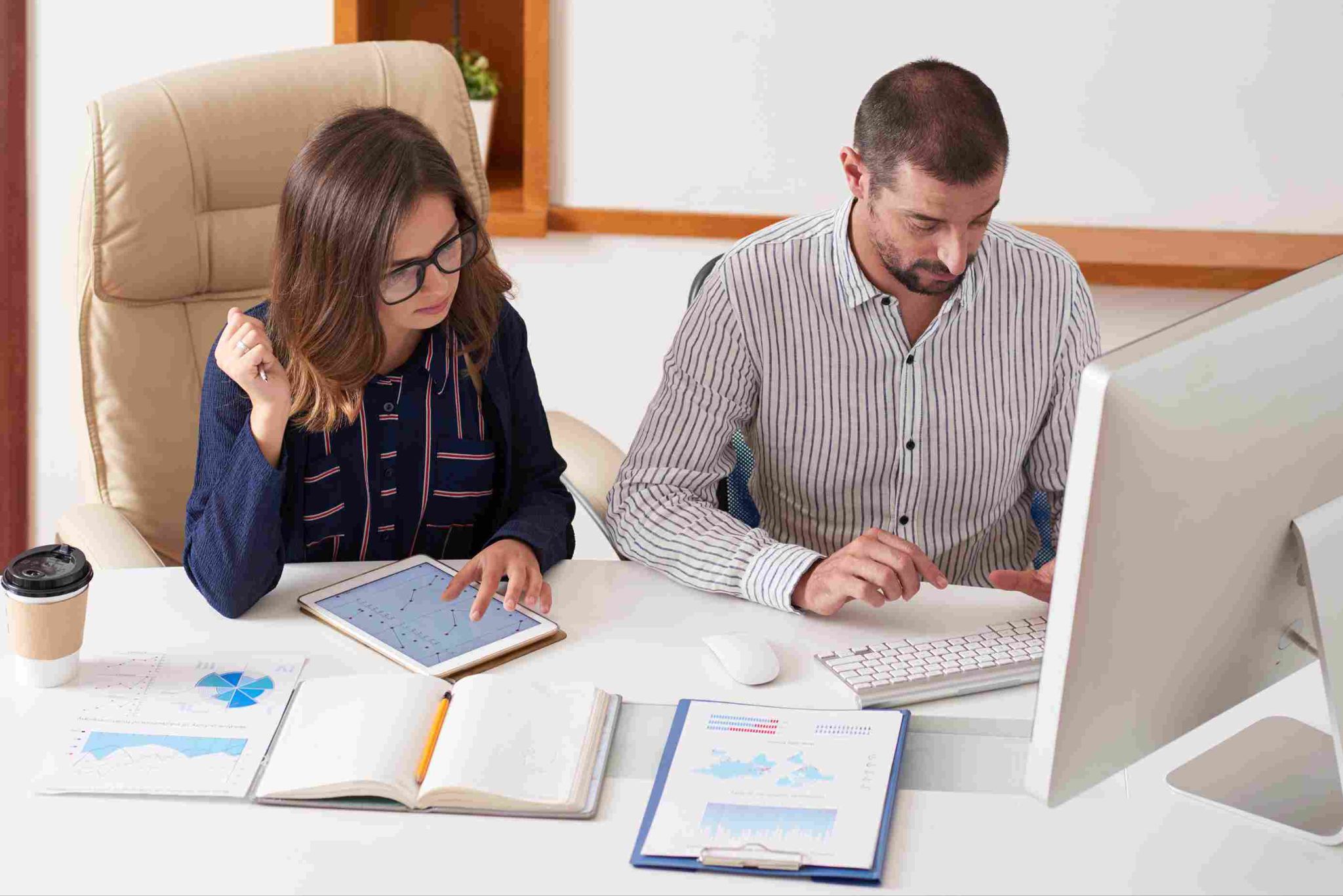Man and woman reviewing information on a tablet and computer at a desk