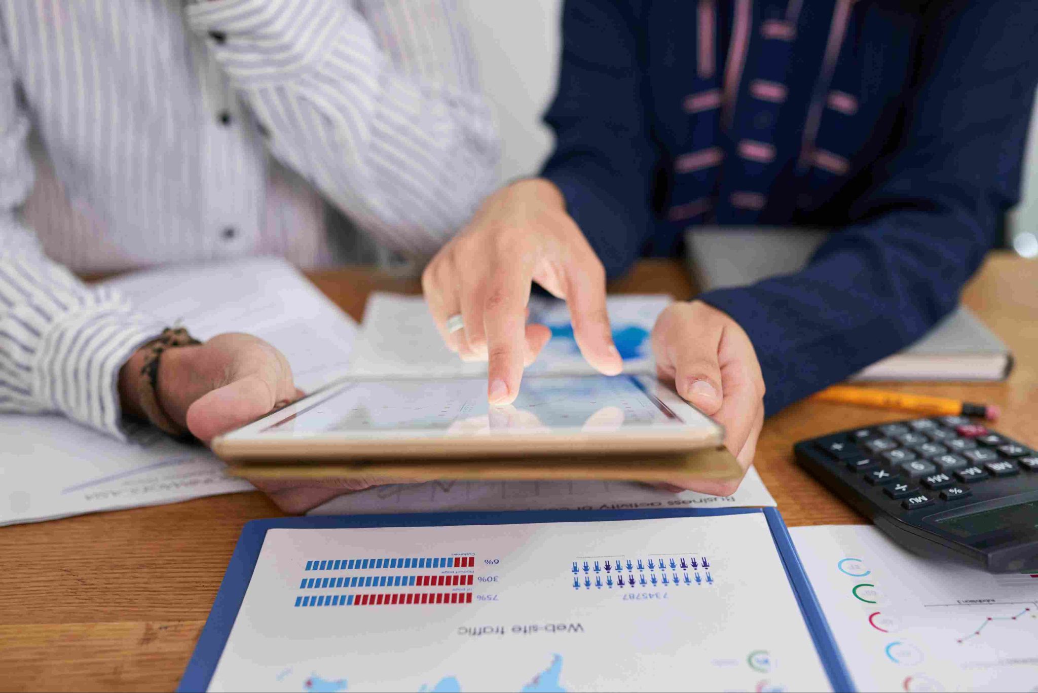 Hands pointing at a tablet showing data, with charts and graphs on paper below