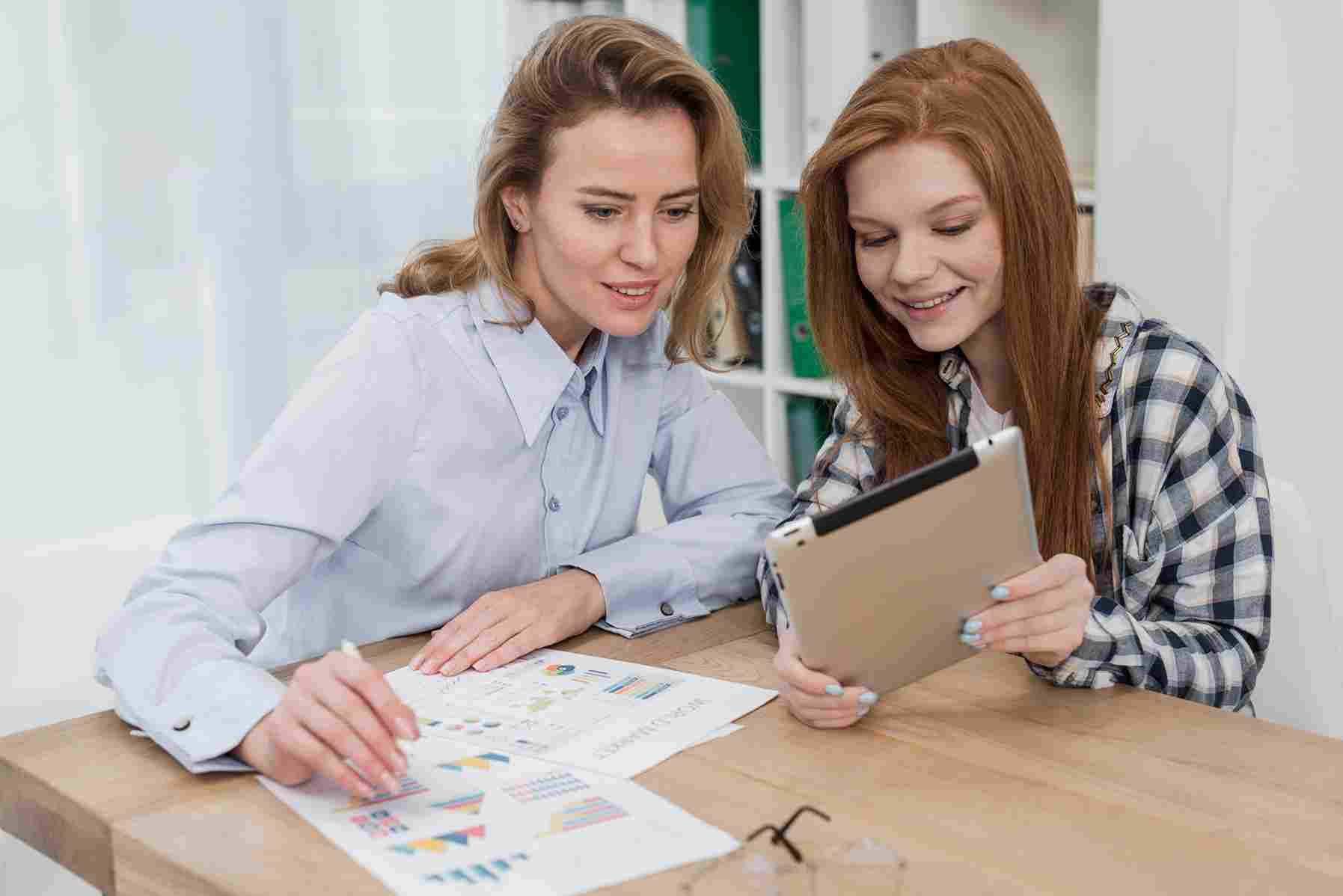 Two women reviewing payroll and financial documents on a tablet