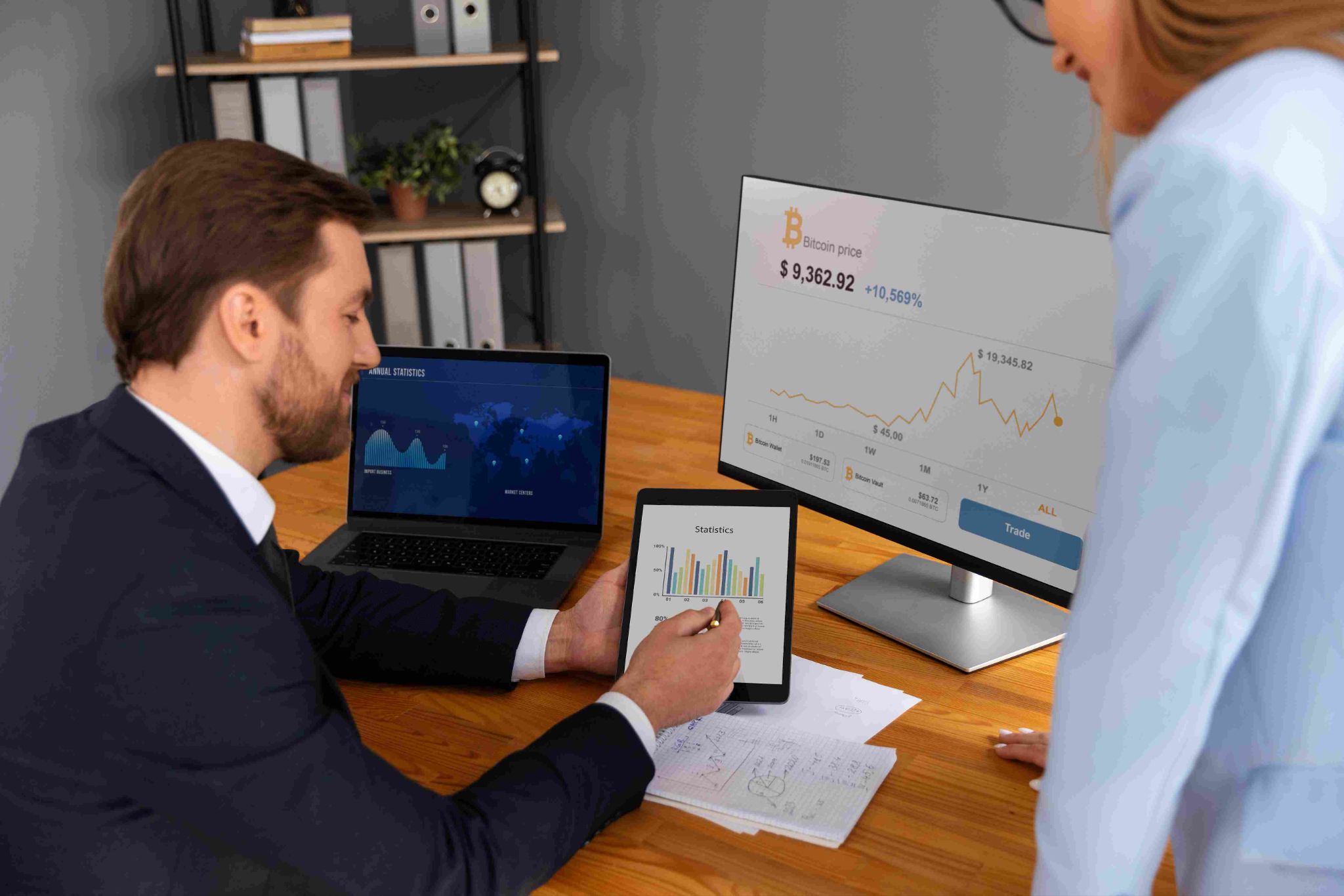 Man and woman looking at a laptop and monitor with charts