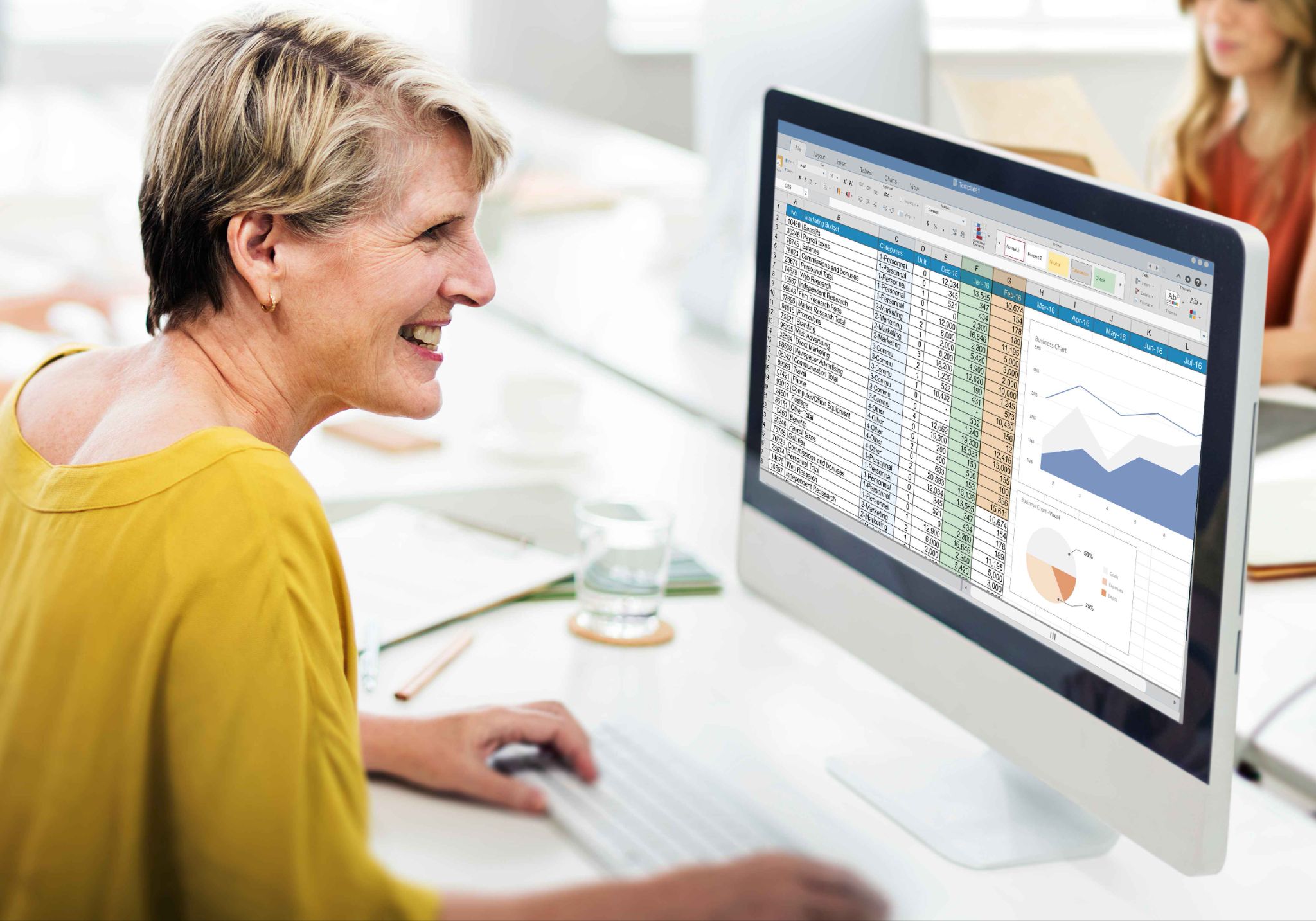 An older woman smiling while using a computer with a spreadsheet