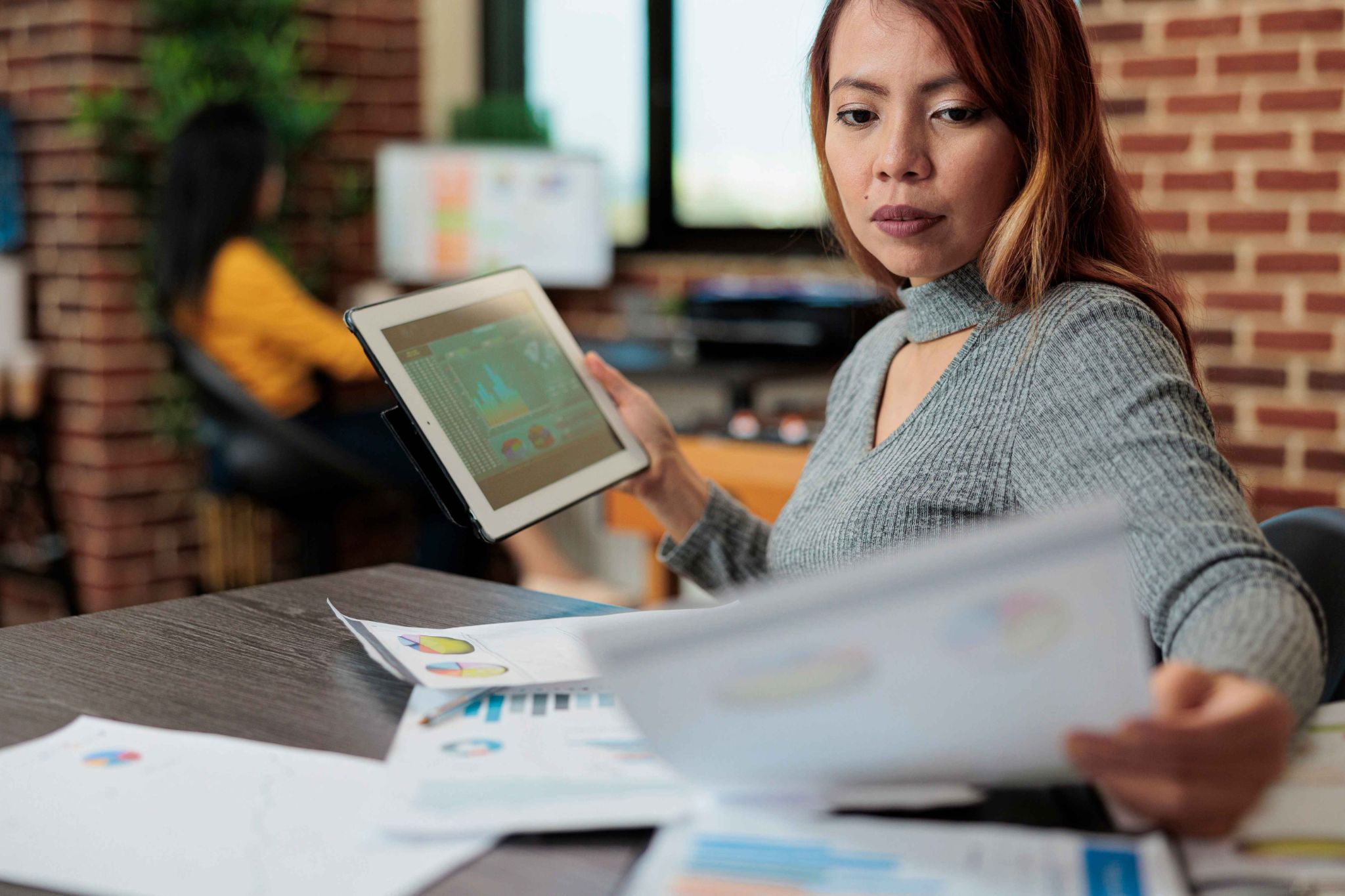 A woman looking thoughtfully at a tablet and papers