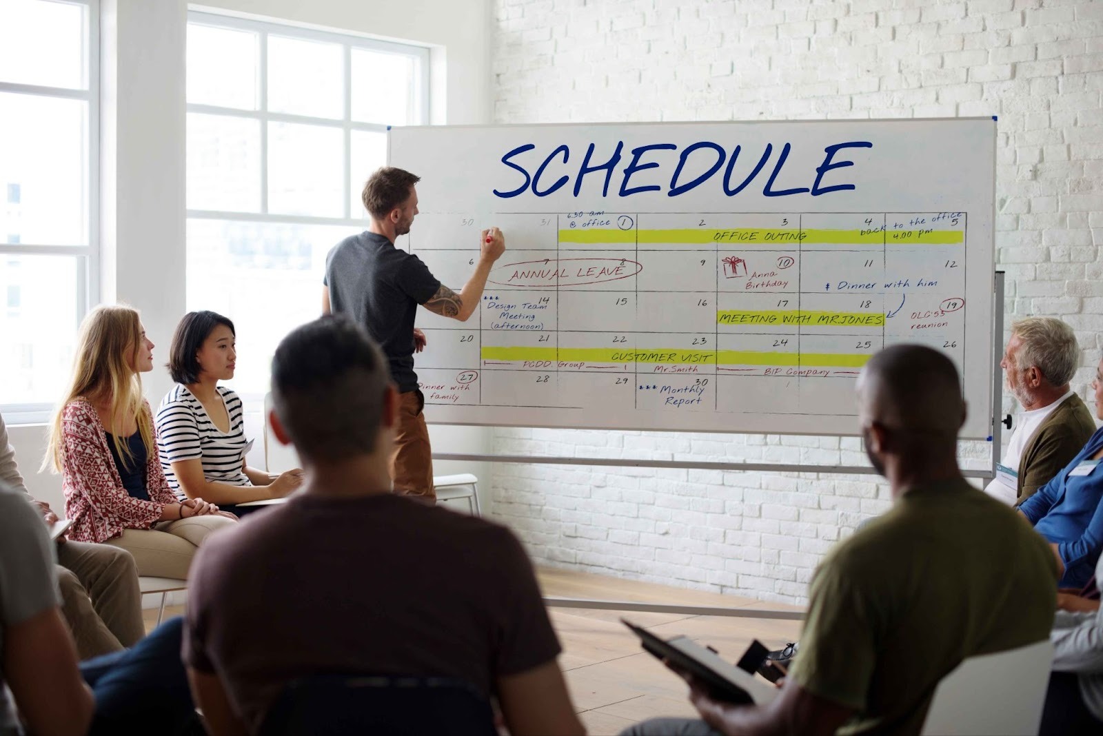 Group of people looking at a whiteboard with SCHEDULE written on it