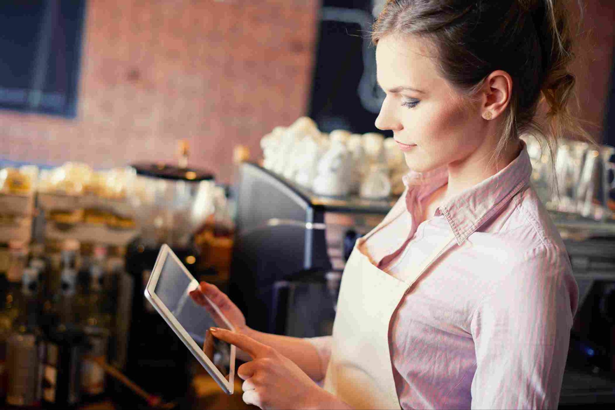 Woman in an apron using a tablet time clock kiosk