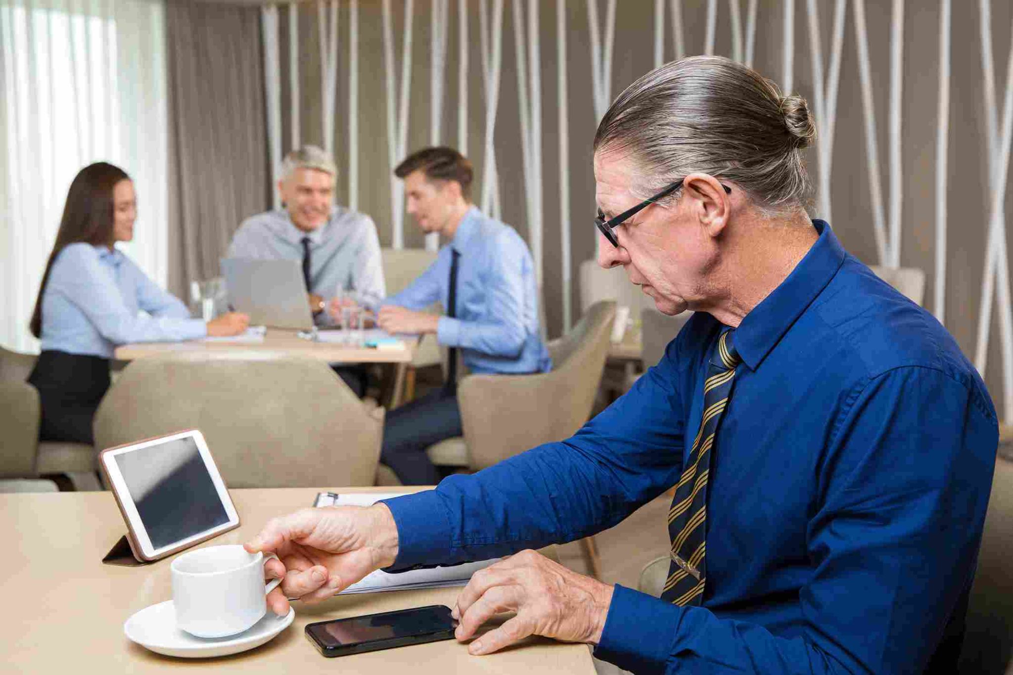 Older man with glasses looking at a phone in an office setting