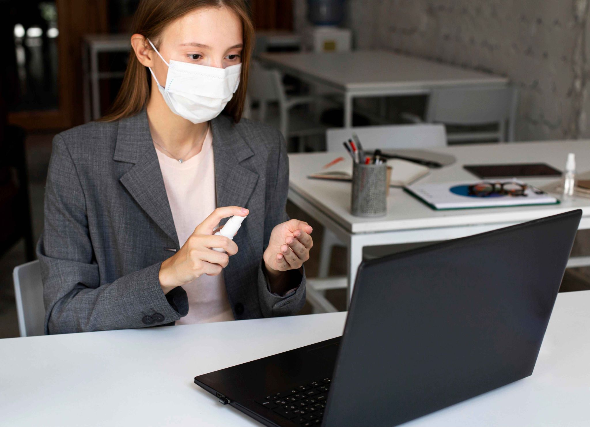 Woman using hand sanitizer at desk with laptop