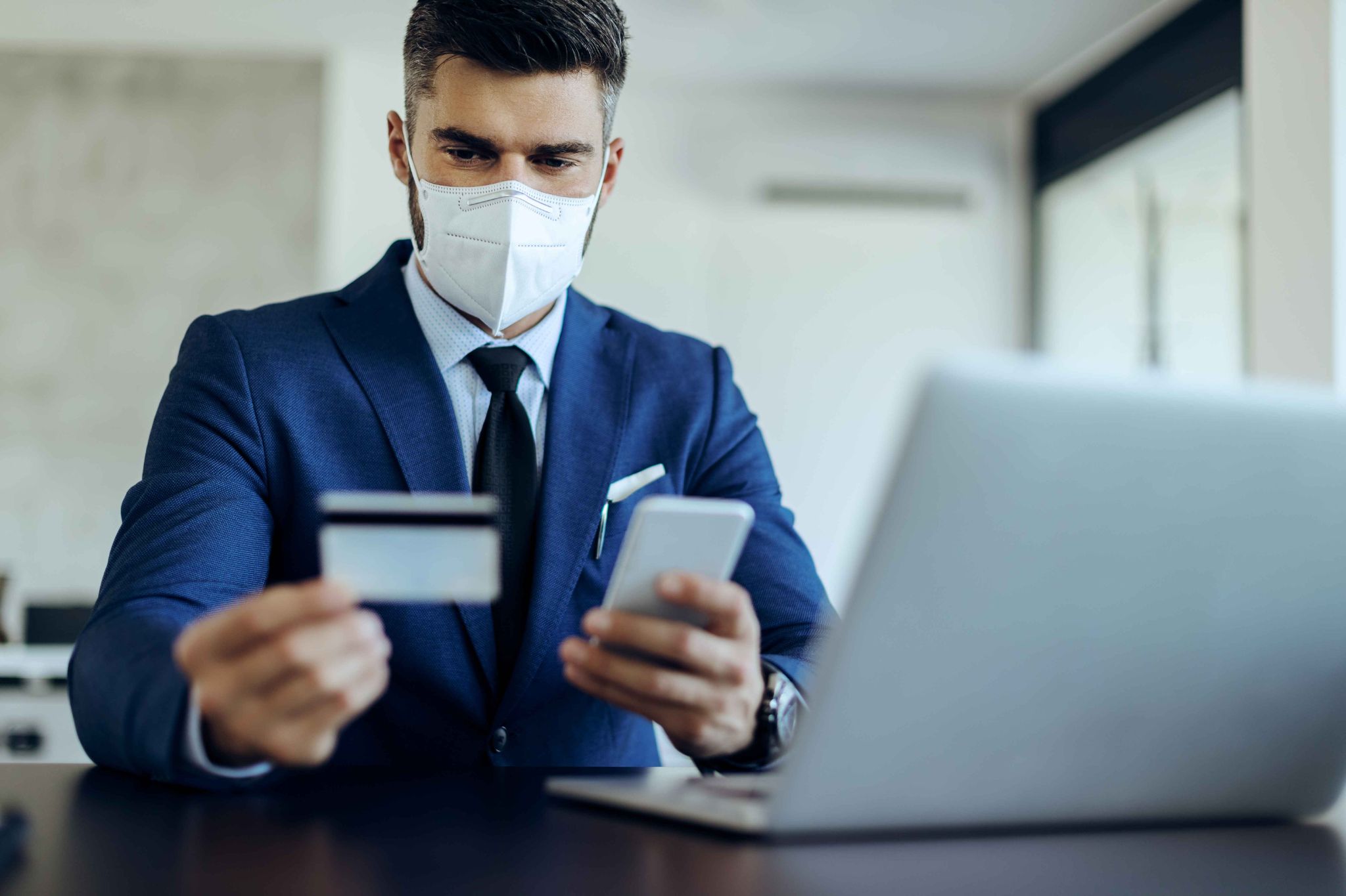 Man in a suit and mask holding a tablet and phone