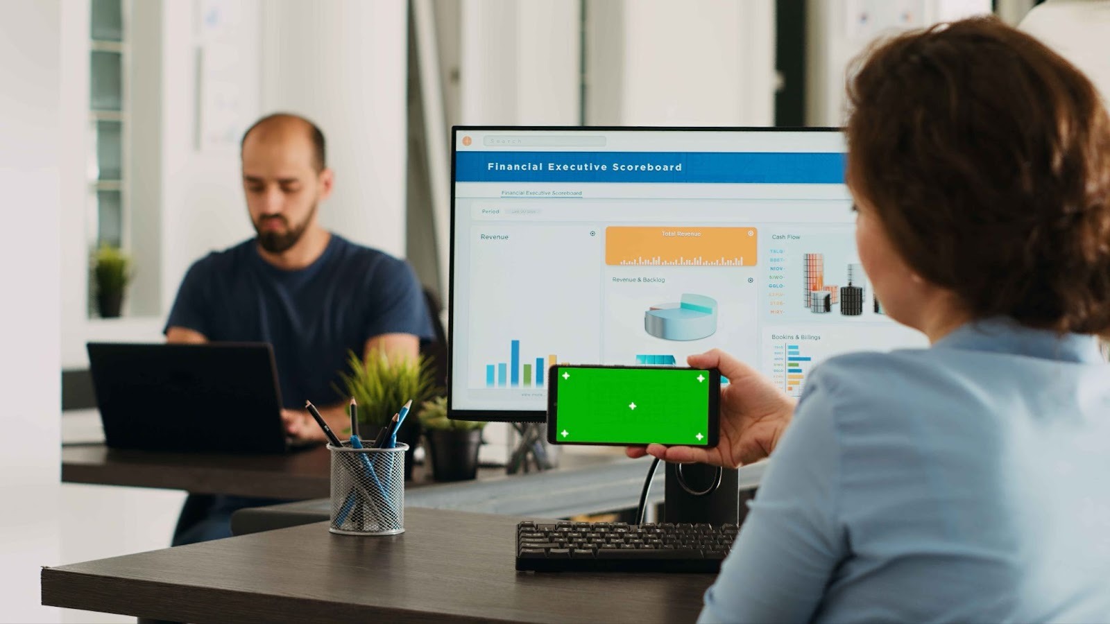 People looking at a financial executive scoreboard on a monitor and phone