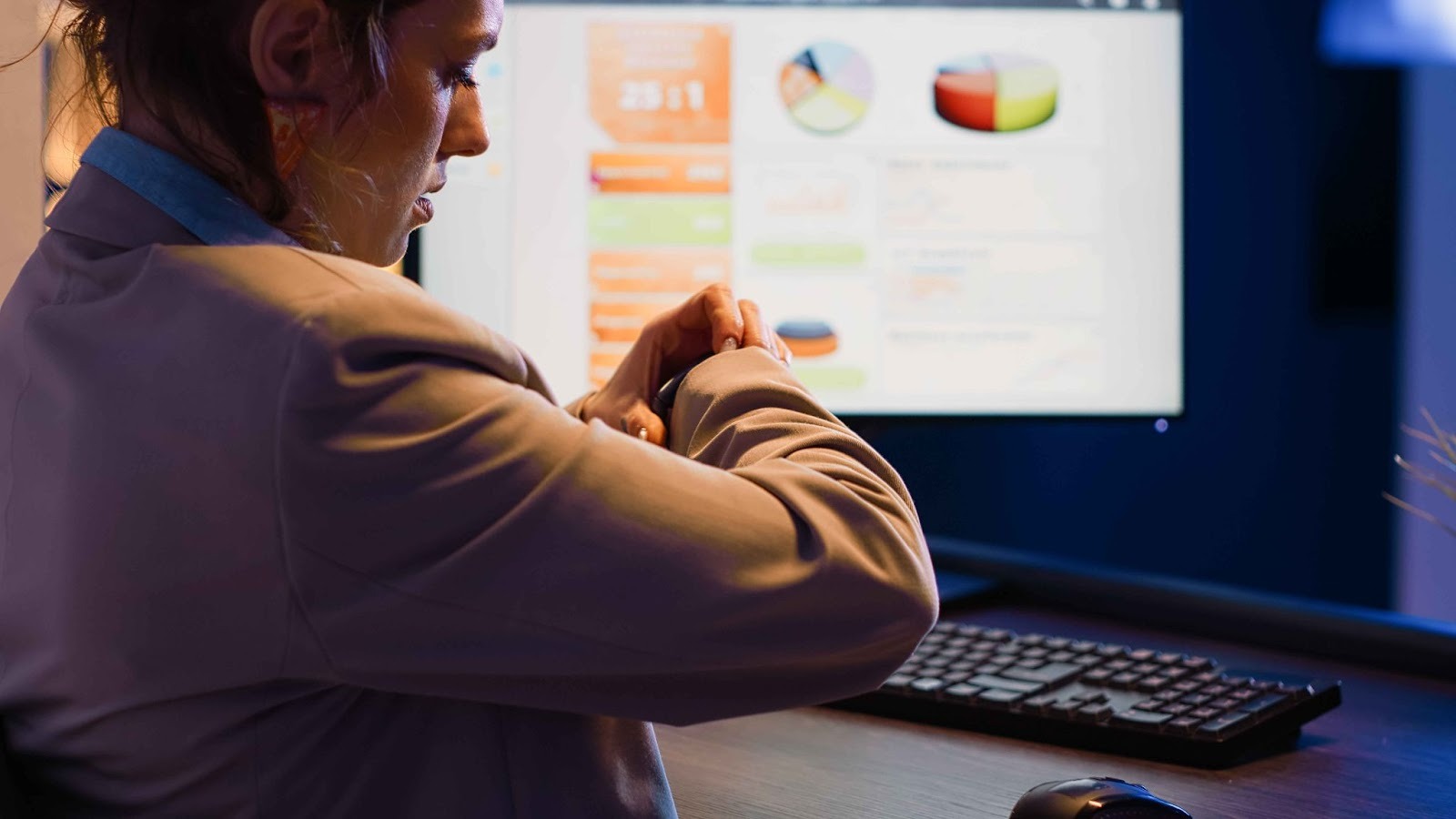 Woman looking at her watch in front of a computer monitor