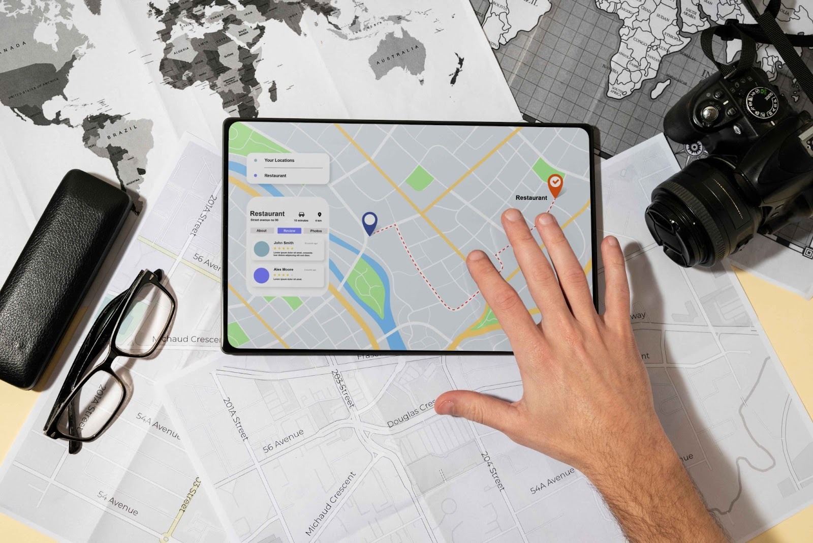 Hands using a tablet with a map interface next to a camera and glasses