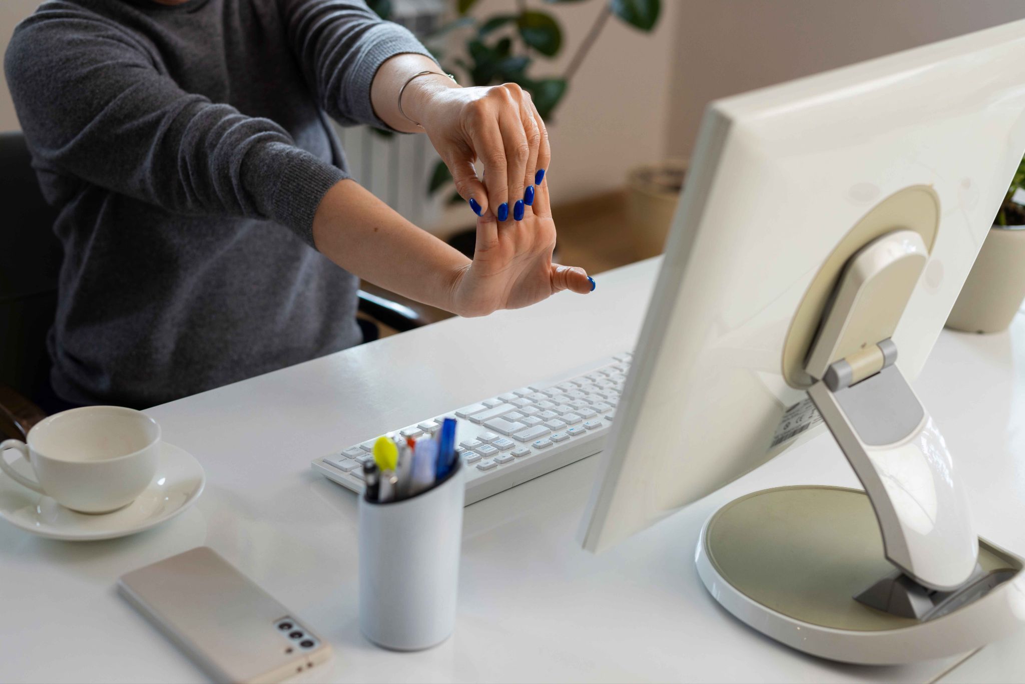 Person stretching arms at their desk in front of a computer monitor