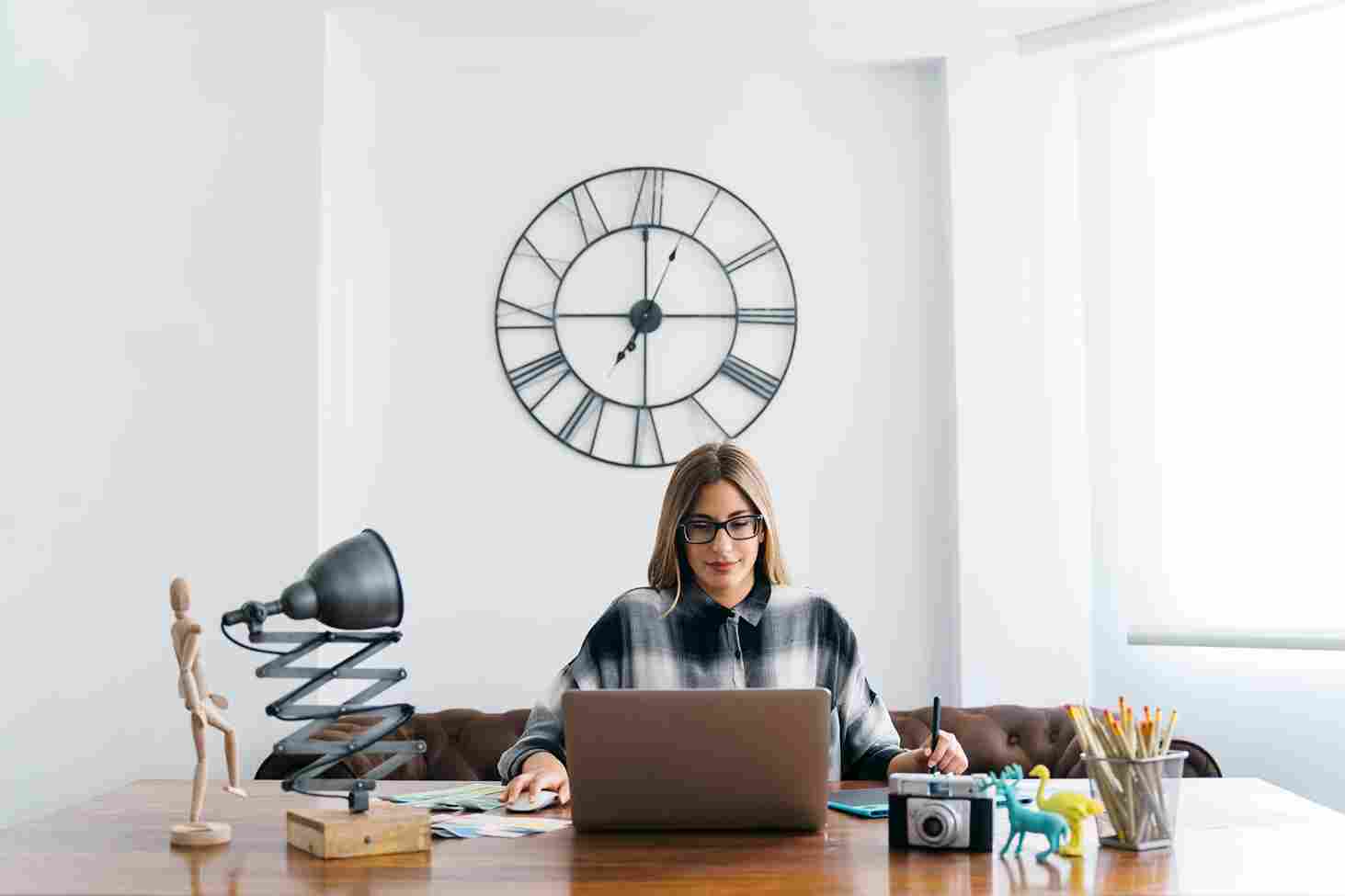Woman working at desk with large wall clock behind her