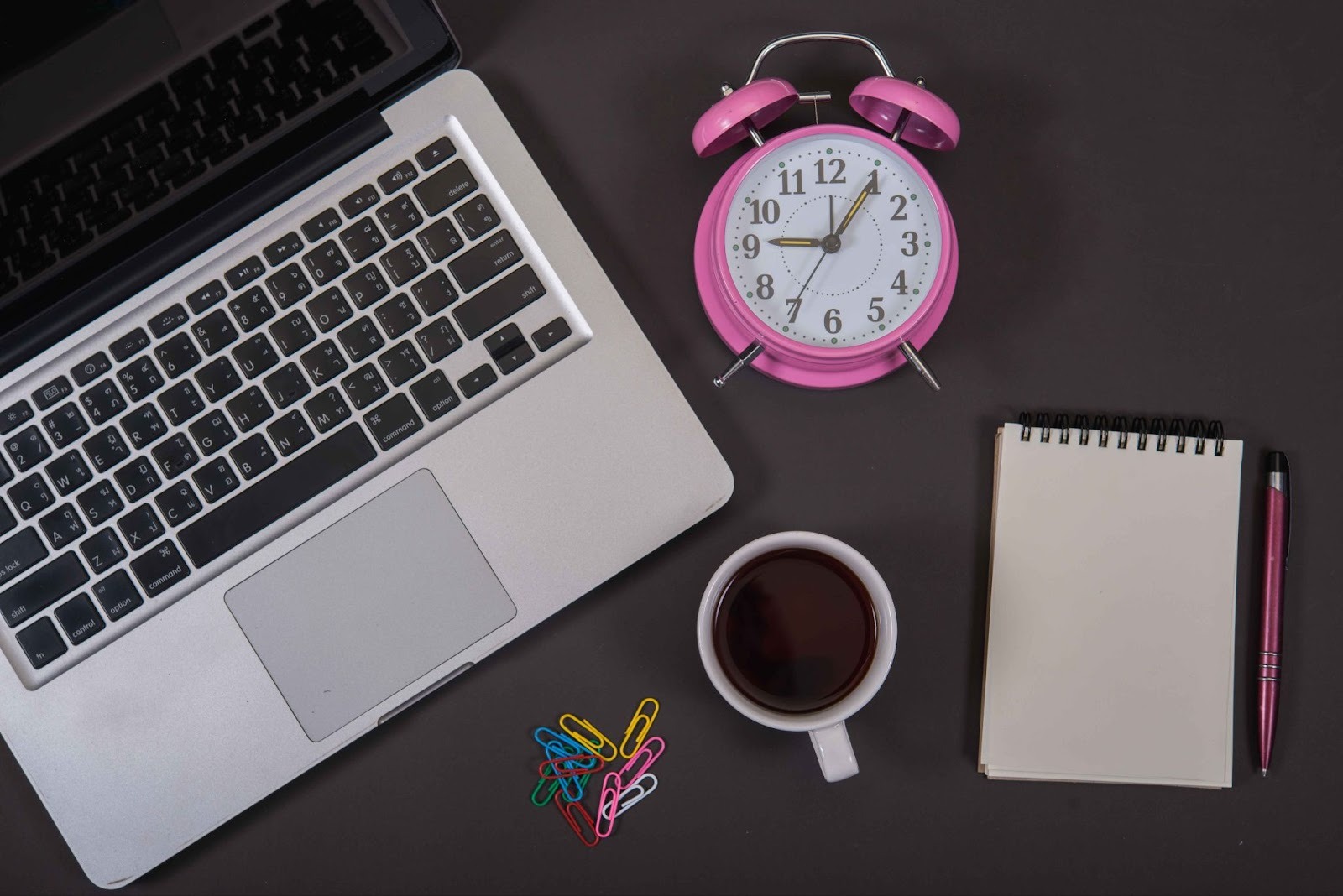 Laptop, clock, coffee, and notebook on a desk